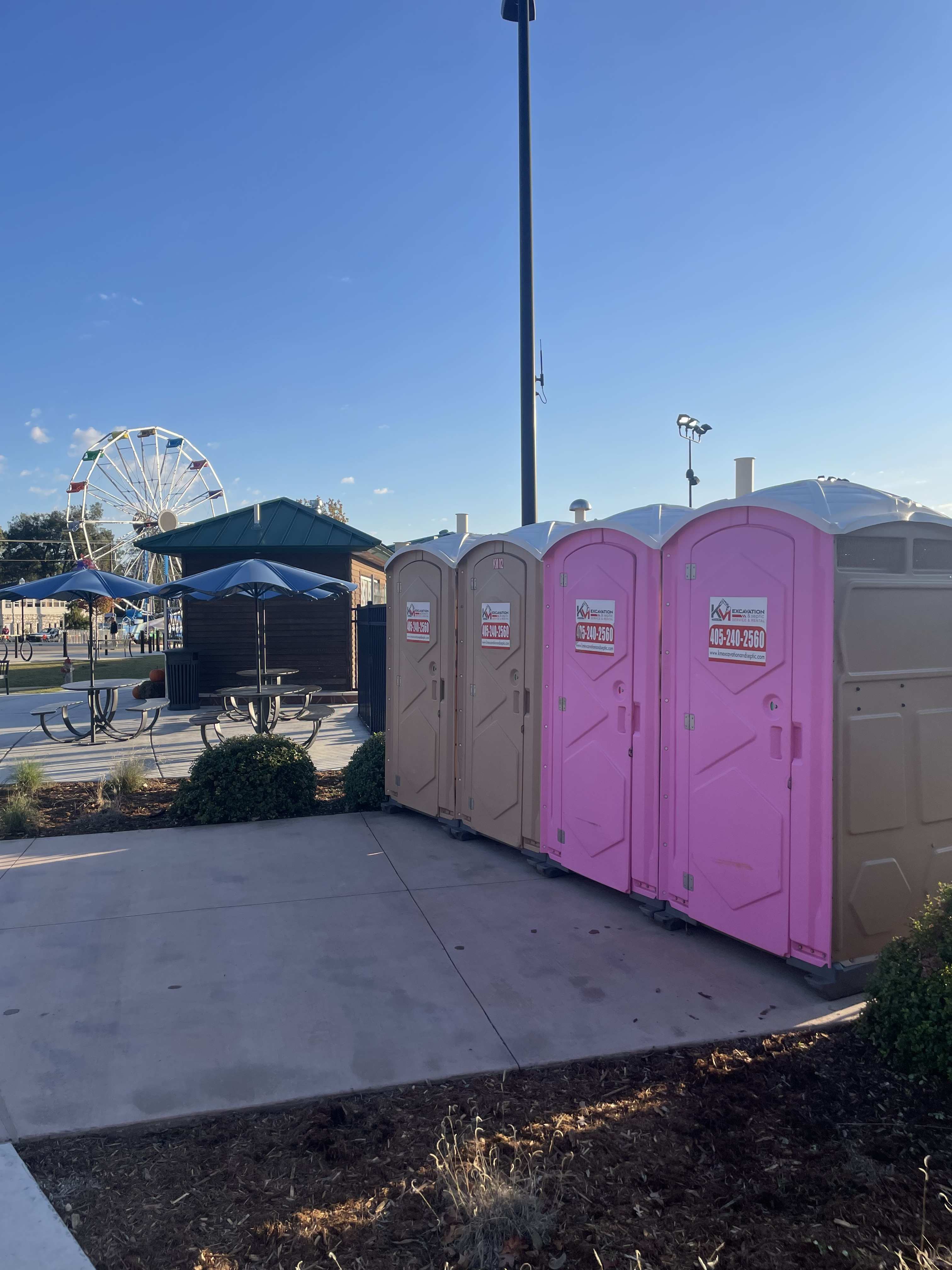 K&M porta potties at a fairground with a ferris wheel in the background